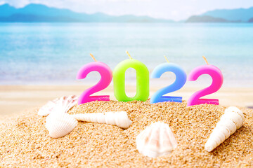 candle number 2022 and sea shell over blurred blue sea and sand beach with clear blue sky on day...