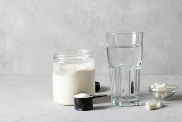 Collagen powder in a jar and measuring spoon, collagen capsules and a glass of water on a light gray background. Healthy and antiage concept