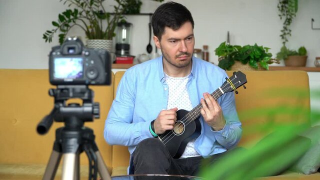 Video tutorial, online music training. Young male blogger records video at home playing guitar. Online music trainer