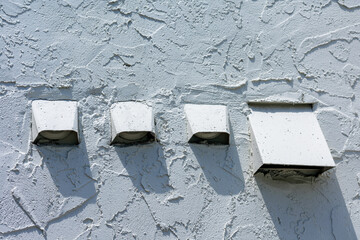Several air exhaust vents with flapper and screen on white stucco wall of residential building.