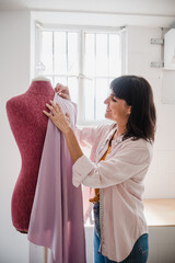Hispanic adult woman fashion designer working with mannequin in studio