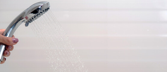 Jets of water flow from the shower head in the female hand. Panoramic photo.