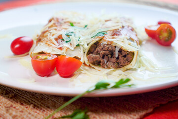 Pancakes with meat, in tomato sauce and cheese, with cilantro and grated cheese on top, and some cherry tomatoes on the plate.