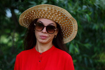 Portrait of a pensive and funny woman in a red blouse on a green nature background.