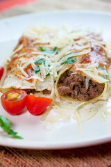 Pancakes with meat, in tomato sauce and cheese, with cilantro and grated cheese on top, and some cherry tomatoes on the plate.