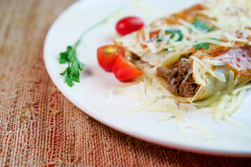 Pancakes with meat, in tomato sauce and cheese, with cilantro and grated cheese on top, and some cherry tomatoes on the plate.