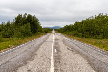 endless gravel road leading trhough forest and tundra wilderness in a straight line to the horizon