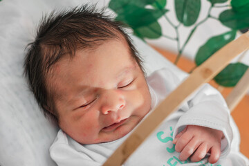 Beautiful newborn baby (4 days old), sleeping in bamboo fiber basket and surrounded by green leaves. close-up top view, healthy doctor concept