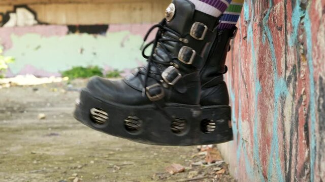 Teenager girl slide with rough boots striped stockings sits on ornate wall of an abandoned building Slow motion. Alternative in youth. An alternative in youth. Hipster, freak, emo, grunge