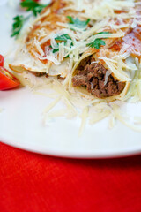 Pancakes with meat, in tomato sauce and cheese, with cilantro and grated cheese on top, and some cherry tomatoes on the plate.
