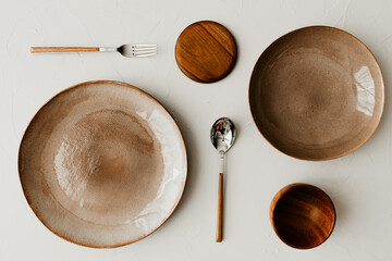 Two different size plate with a spoon and fork on beige background. Flat lay, top view. Brown and natural color plates. Textured grainy pattern on the plates. 