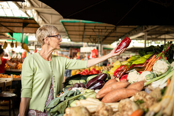 Elderly woman buying fresh organic vegetables at market place for healthy nourishment.