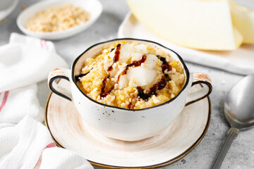 Millet porridge with melon slices and walnuts in a ceramic bowl on a light gray kitchen table closeup. Delicious and healthy breakfast