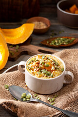 Millet porridge with pumpkin slices and seeds, walnuts in a ceramic bowl in a rustic style close-up. Delicious and healthy autumn breakfast