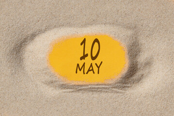 May 10. 10th day of the month, calendar date. Hole in sand. Yellow background is visible through hole. Spring month, day of the year concept