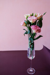 Pink eustoma flowers in a vase or glass on a purple table.
