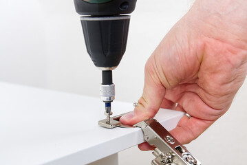 the carpenter screws the hinge on the furniture door. DIY Furniture assembly service concept