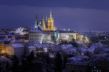 Obraz na płótnie Canvas Prague Castle in Hradcany district with an illuminated street below at night in winter covered with snow captured from Petrin Hill