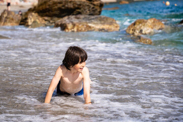 Fototapeta premium Young boy playing alone in waves. Happy child spends summer holidays at the seaside in France.