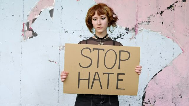 Stop Hate Cardboard Asian Teenager Girl Is Held Holding Sign With Words STOP HATE As Symbolic Expression To Stop Threats, Crime On Wall Background. Protests. Alternative Youth. Problem School