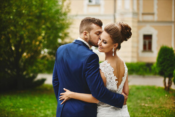 Fototapeta premium A handsome man in a trendy blue suit hugging and kissing a beautiful model woman in a wedding dress. A happy couple of newlyweds hugging after the outdoor wedding ceremony