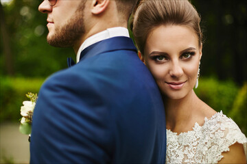 A happy couple of newlyweds hugging and looking in the camera. Beautiful model girl in a wedding dress and handsome man in trendy blue suit