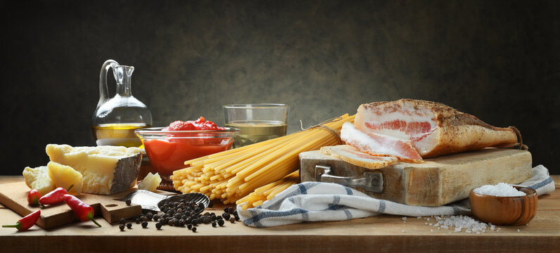 Ingredients for Amatriciana pasta. Bucatini, guanciale, peeled tomatoes, pecorino cheese, extra virgin olive oil, white wine, chilli and salt. Still life, gray background, space for text. 