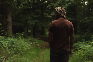 Blonde man in brown t-shirt on a forest path in summer. Rear vie