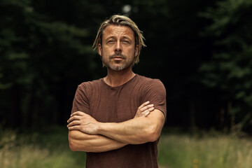 Blonde man with his arms folded and a stubble beard in a brown t