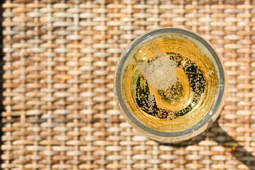 Close up viewing looking down on a glass of champagne on a wicker garden table on a summer evening.