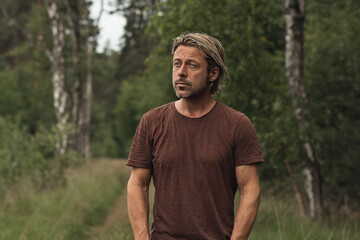 Naklejka na ściany i meble Blonde man with a stubble beard in a brown t-shirt on a forest p