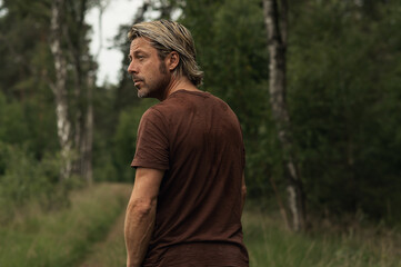 Blonde man with a stubble beard in a brown t-shirt looks over hi