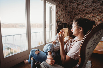Mother breastfeeding baby on chair in vintage room looking out on lake