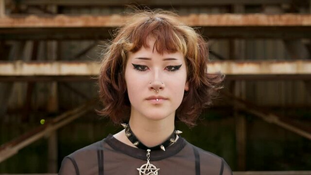 Asian teen girl with short haircut walks and looks directly camera on wall background of an abandoned building sunny day summer. An alternative in youth. Protests