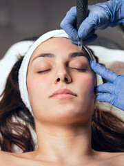 Cosmetologist making micropigmentation injection on face for rejuvenation while lying on a...