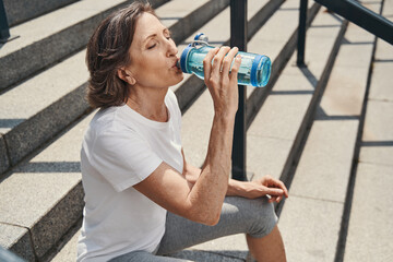 Active aged woman quenching thirst on steps