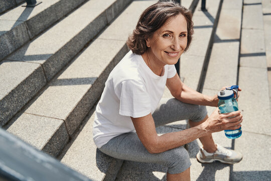 Joyful athletic aged woman relaxing on stairs outdoors
