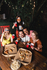 High angle view of african american man hugging cheerful friends with pizza and beer during outdoor summer party