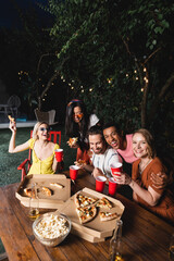 Happy multiethnic friends with beer, pizza and popcorn having fun during summer party