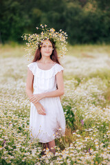 Fototapeta na wymiar Beautiful girl in a wreath of daisies in a white dress in a field of daisies.
