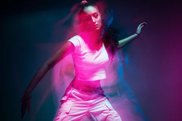 Foto op Canvas Colourful portrait of young mixed race girl dancing in studio. Long exposure. Colored neon light. © Georgii