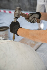 Detail of artist's hands sculpting marble with hammer and chisel