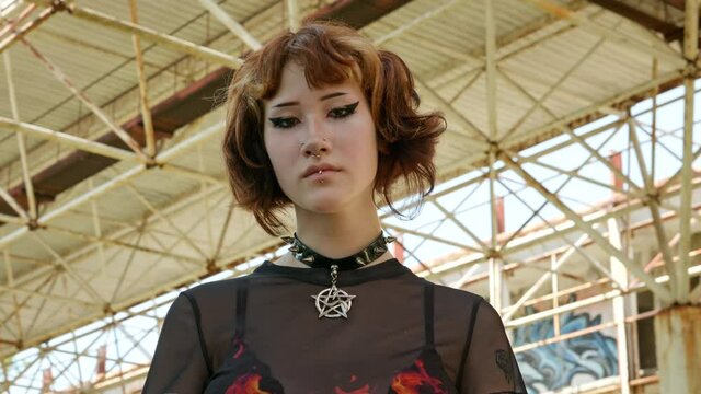 Asian teen girl looks directly camera with short haircut on wall background slide turn of an abandoned building sunny day summer. Portrait An alternative in youth. Protests. Freedom. Freak