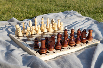 Wooden chessboard with pieces in the park on green grass.