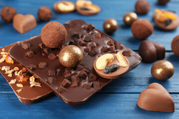 Different delicious chocolate candies and bars on blue wooden table, closeup