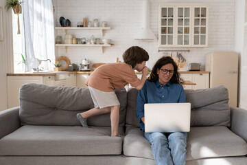 Frustrated young woman, entrepreneur or remote worker work on laptop tired stressed of hyperactive disobedient little kid distract mom from business occupation in home office on sofa in living room