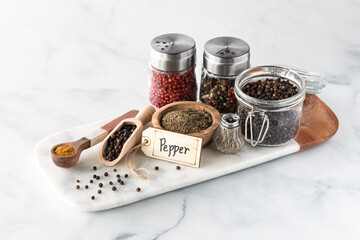 An arrangement of different types of pepper in various containers on a marble slab.