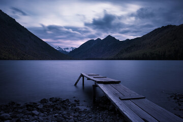 Long exposure evening mountain landscape. Old wooden pier on the lake. Mountain sunset and dramatic sky.