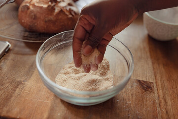 Close up of a brown hand testing freshly milled flour in a glass mixing bowl