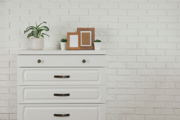 Modern chest of drawers with decor near white brick wall. Space for text
